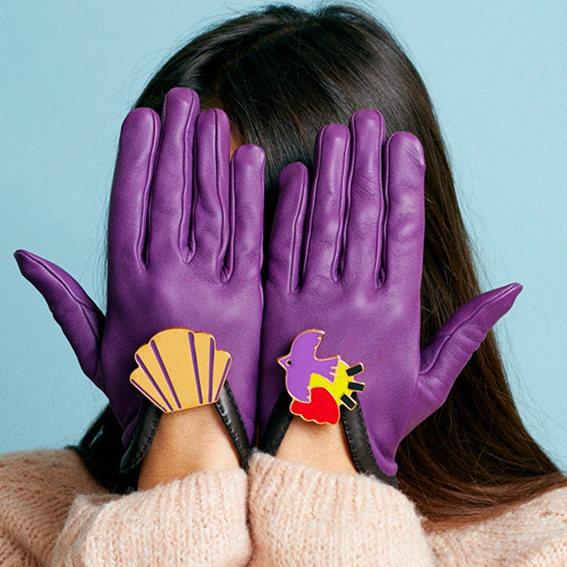 Bijou clip en forme de coquillage doré et violet porté sur gant en cuir violet