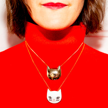 Jewel clip in the shape of a golden cat worn on a necklace and red jumper