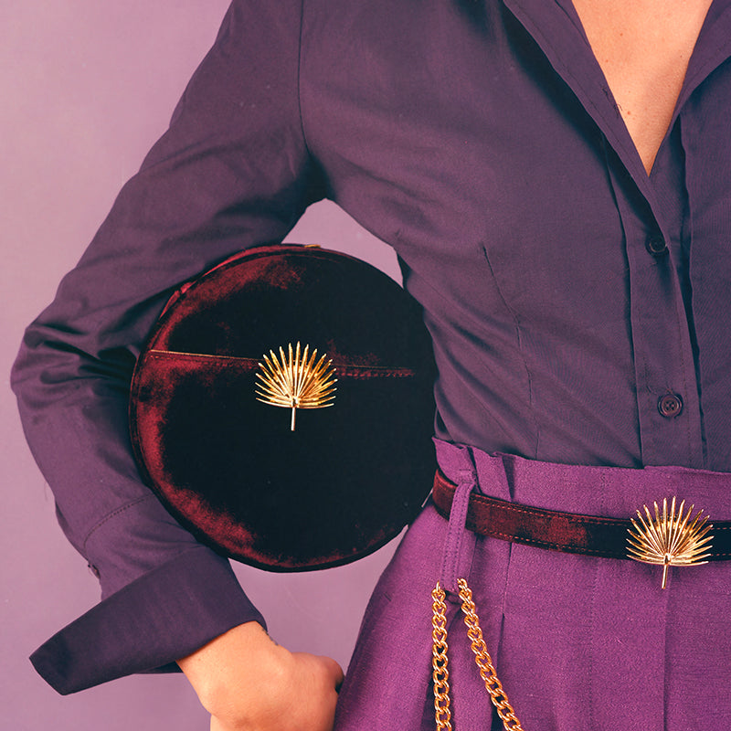Gold palm tree clip jewel worn on velvet bag and purple trouser belt