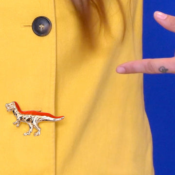 Jewel clip in the shape of a golden and orange T-rex dinosaur on a yellow jacket buttonhole